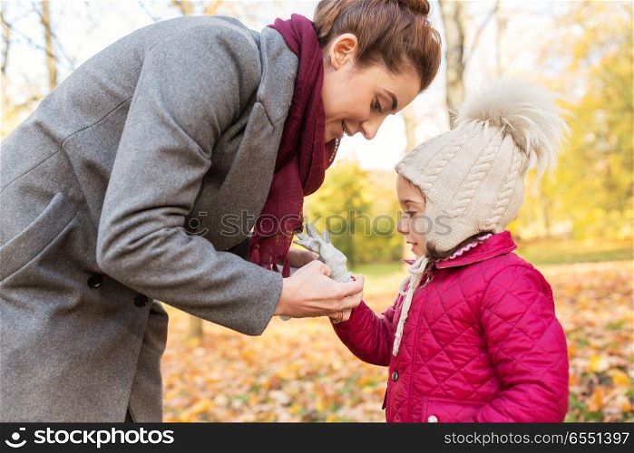 family, season and people concept - happy mother helping little daughter with glove at autumn park. happy mother and little daughter at autumn park. happy mother and little daughter at autumn park