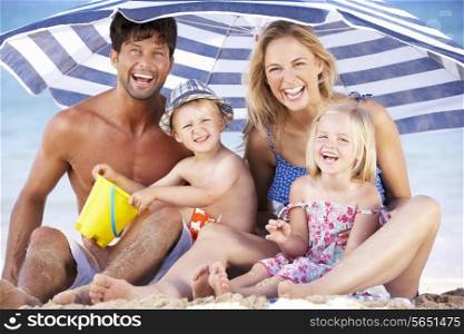 Family Sheltering From Sun Under Beach Umbrella