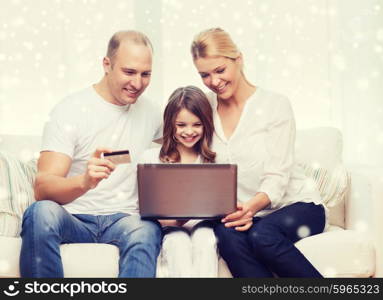 family, shopping, technology and people concept - happy family with laptop computer and credit card over snowflakes background