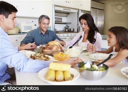 Family Sitting Around Table Saying Prayer Before Eating Meal