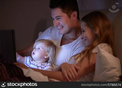 Family Sitting In Bed Looking At Digital Tablet