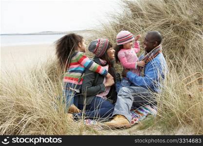 Family Sitting In Dunes Enjoying Picnic On Winter Beach