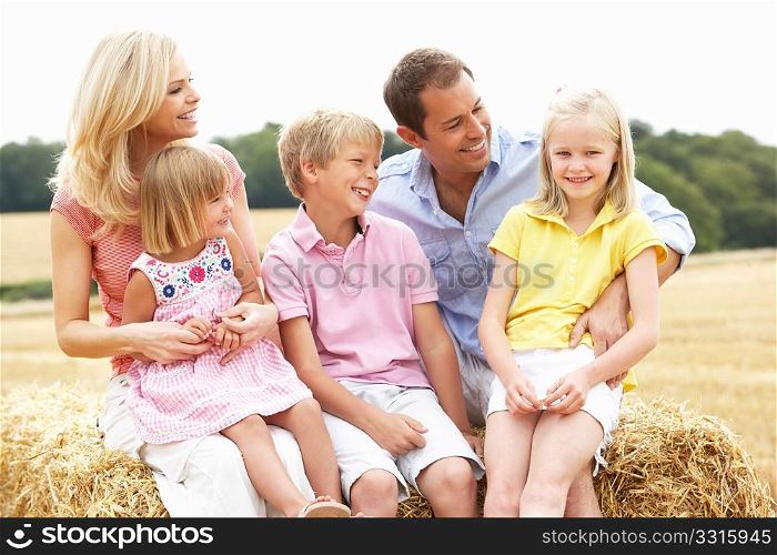 Family Sitting On Straw Bales In Harvested Field