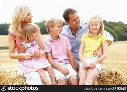 Family Sitting On Straw Bales In Harvested Field