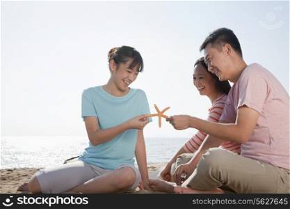 Family sitting on the beach by the ocean holding a starfish