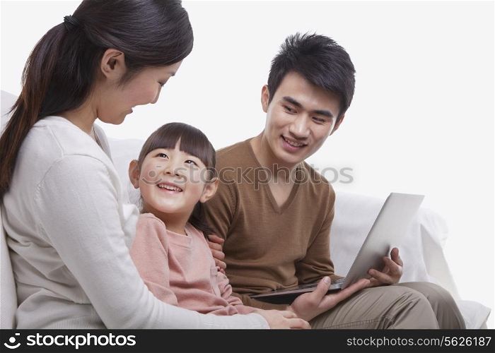 Family sitting on the sofa using laptop, mother looking at daughter, studio shot