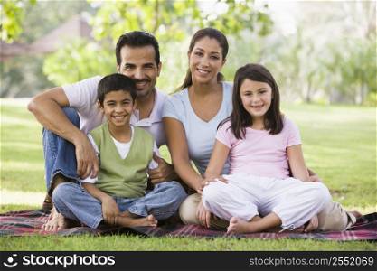 Family sitting outdoors in park smiling (selective focus)