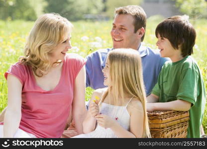 Family sitting outdoors with picnic basket smiling