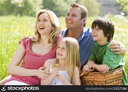 Family sitting outdoors with picnic basket smiling