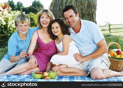 Family sitting outdoors with picnic smiling