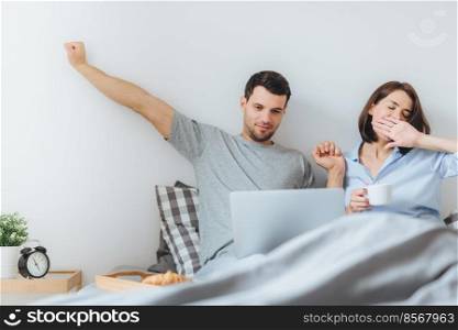 Family spend time together in bedroom, stretch and yawn as get up early, do remote work on laptop computer, use free wifi connection, drink coffee, being busy. Morning and awakening