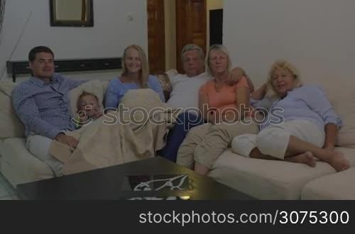Family spending quiet evening at home. Parents, child and grandparents sitting on the sofa and watching TV