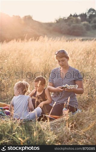 Family spending time together on a meadow, close to nature, parents and children playing together, making coronet of wild flowers. Candid people, real moments, authentic situations
