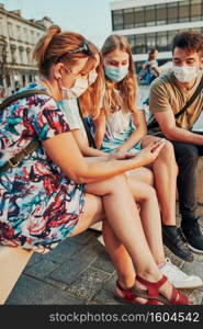 Family spending time together sitting in the city center. Girls wearing the face masks to avoid virus infection and to prevent the spread of disease in time of coronavirus