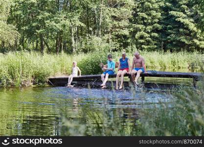 Family spending time together sitting on a bridge over a lake, among the trees, close to nature, during summer vacations. Candid people, real moments, authentic situations