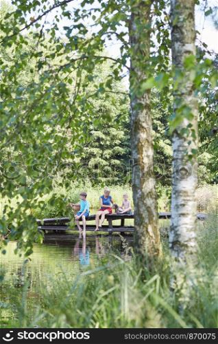 Family spending time together sitting on a bridge over a lake, among the trees, close to nature, during summer vacations. Candid people, real moments, authentic situations