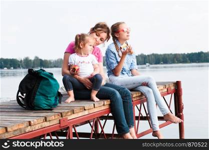 Family spending vacation time together having a snack sitting on jetty over the lake on sunny day in the summertime