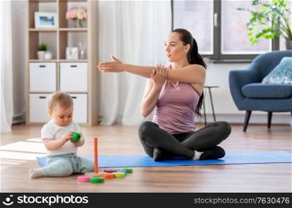 family, sport and motherhood concept - happy mother exercising on mat and little baby playing with toys at home. happy mother with little baby exercising at home