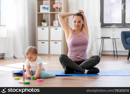 family, sport and motherhood concept - happy smiling mother exercising on mat and little baby playing with toys at home. happy mother with little baby exercising at home