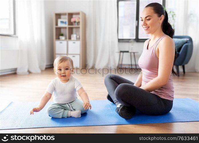 family, sport and motherhood concept - happy smiling mother with little baby sitting on exercise mat at home. happy mother with little baby at home