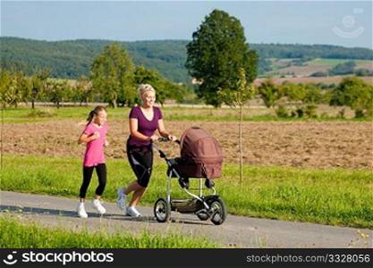Family sport - mother and daughter jogging down a path with a baby stroller at a wonderful sunny day