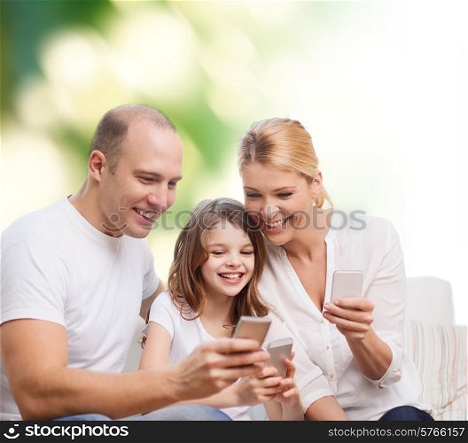 family, summer, technology and people concept - smiling mother, father and little girl with smartphones over green background