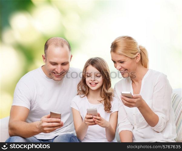 family, summer, technology and people - smiling mother, father and little girl with smartphones over green background
