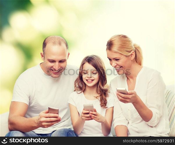 family, summer, technology and people - smiling mother, father and little girl with smartphones over green background