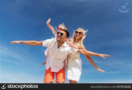 family, summer vacation, adoption and people concept - happy man, woman and little girl in sunglasses having fun over blue sky background
