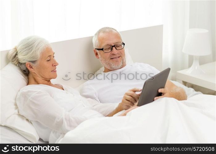 family, technology, age and people concept - happy senior couple with tablet pc computer lying in bad at home