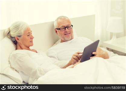 family, technology, age and people concept - happy senior couple with tablet pc computer lying in bad at home