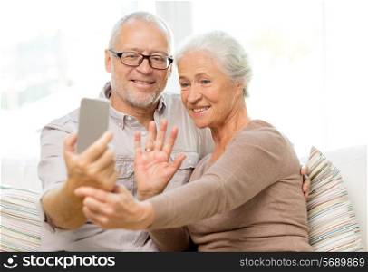 family, technology, age, gesture and people concept - happy senior couple with smartphone making selfie and waving hand at home