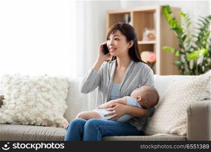 family, technology and motherhood concept - happy smiling young asian mother with sleeping baby calling on smartphone at home. mother with baby calling on smartphone at home. mother with baby calling on smartphone at home
