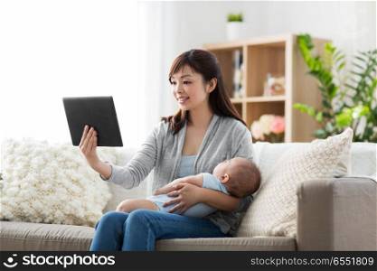 family, technology and motherhood concept - happy smiling young asian mother with sleeping baby and tablet pc computer at home. mother with sleeping baby and tablet pc at home. mother with sleeping baby and tablet pc at home