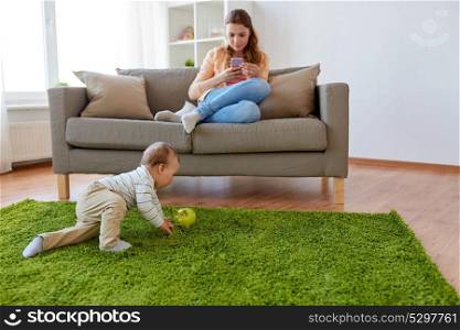 family, technology and motherhood concept - mother with smartphone and baby playing with himself at home. mother with smartphone and baby playing at home