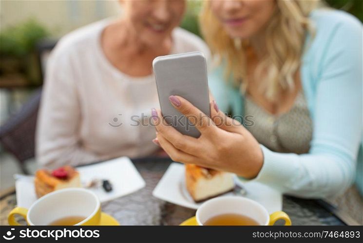 family, technology and people concept - close up of happy smiling adult daughter and senior mother with smartphone taking selfie at cafe. daughter and senior mother taking selfie at cafe