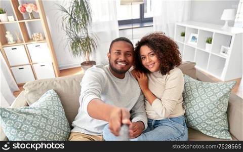 family, technology and people concept - happy african american couple taking picture selfie stick at home. couple taking picture by selfie stick at home