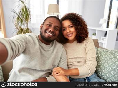 family, technology and people concept - happy african american couple taking selfie at home. african american couple taking selfie at home