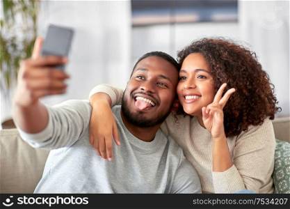 family, technology and people concept - happy african american couple with smartphone taking selfie and showing peace at home. happy couple with smartphone taking selfie at home