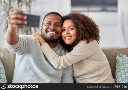family, technology and people concept - happy african american couple with smartphone taking selfie at home. happy couple with smartphone taking selfie at home