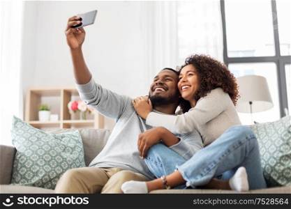 family, technology and people concept - happy african american couple with smartphone taking selfie at home. happy couple with smartphone taking selfie at home