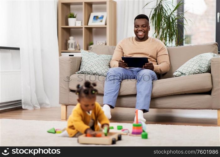 family, technology and people concept - happy african american father with tablet pc computer and baby daughter playing toy blocks at home. happy father with tablet pc and baby at home