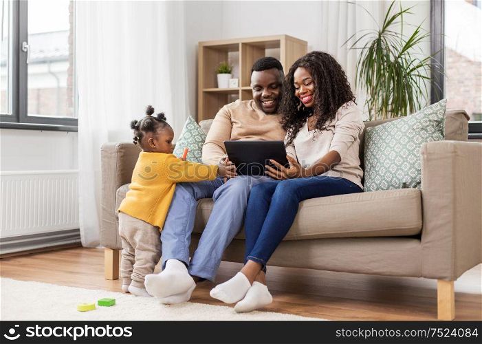 family, technology and people concept - happy african american mother, father and baby daughter with tablet pc computer at home. african american family with tablet pc at home