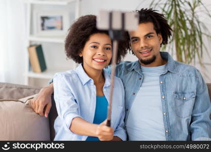 family, technology and people concept - happy couple with smartphone and selfie stick taking picture at home. happy couple with smartphone taking selfie at home