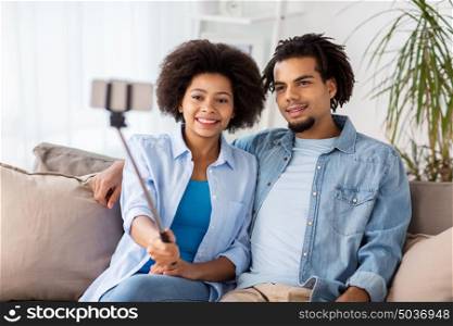 family, technology and people concept - happy couple with smartphone and selfie stick taking picture at home. happy couple with smartphone taking selfie at home
