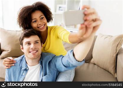 family, technology and people concept - happy couple with smartphone taking selfie at home. happy couple with smartphone taking selfie at home