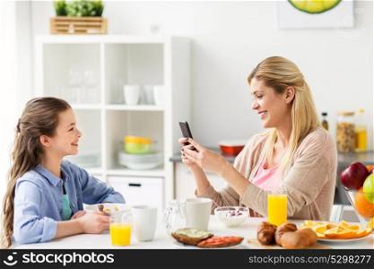 family, technology and people concept - happy girl and mother with smartphone having breakfast at home. family with smartphone having breakfast at home