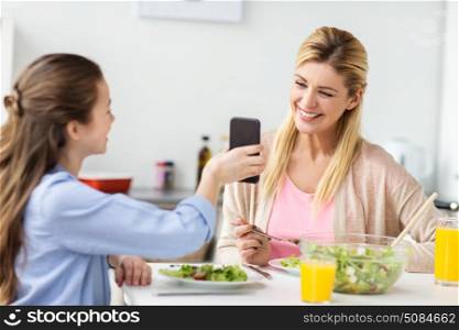 family, technology and people concept - happy mother and daughter with smartphone having dinner at home kitchen. happy family with smartphone having dinner at home. happy family with smartphone having dinner at home