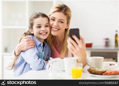 family, technology and people concept - happy mother and daughter with smartphone having breakfast and taking selfie at home kitchen. happy family taking selfie by smartphone at home. happy family taking selfie by smartphone at home