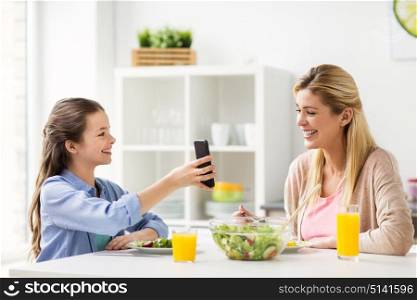 family, technology and people concept - happy mother and daughter with smartphone having dinner at home kitchen. happy family with smartphone having dinner at home